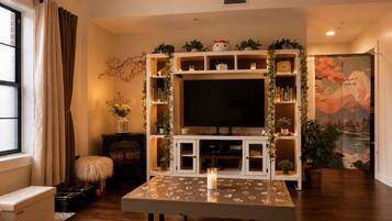 A living room with a TV, wooden cabinets, a table with a candle, and a large window with curtains.