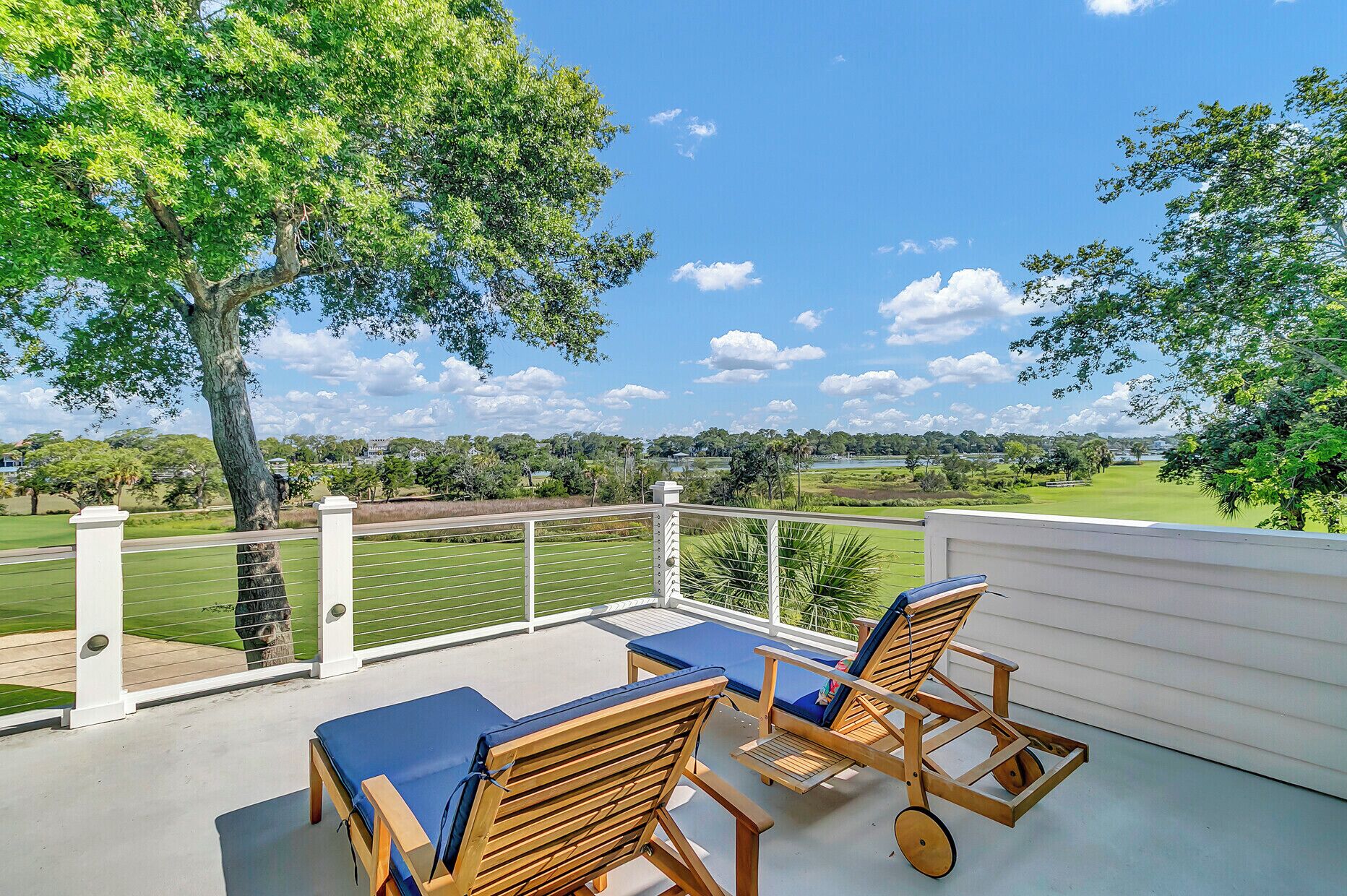 Un balcon avec des chaises et une table en bois, donnant sur un terrain de golf et un lac.