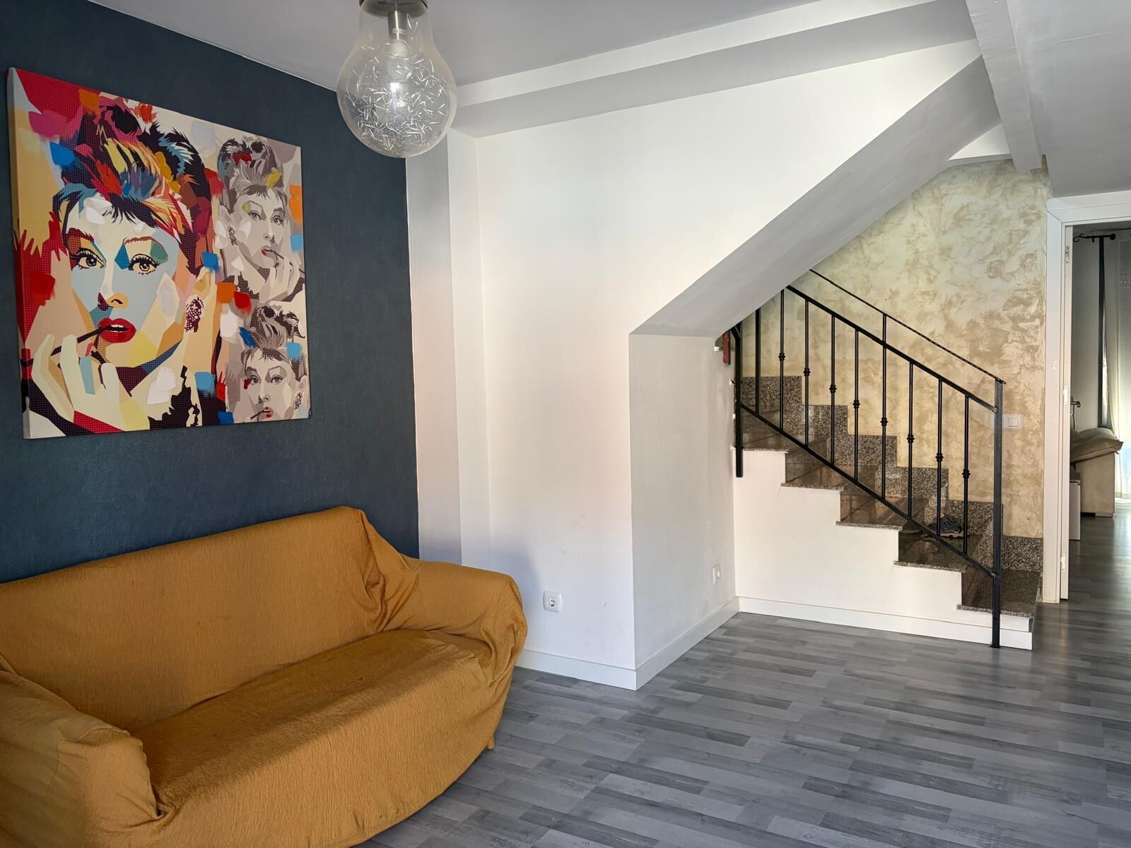 Una sala de estar moderna con un sofá, una escalera y un cuadro de colores en la pared.