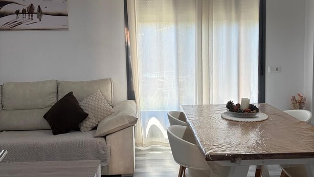 A modern living room with a sofa, a dining table with chairs, a coffee table, and a painting on the wall.