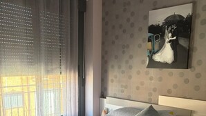 A bedroom with a large bed, a nightstand, a window with curtains, and a wall-mounted picture.