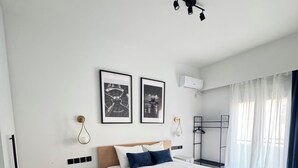 Ein modernes Schlafzimmer mit einem Holzbett, einer roten 'Check-In'-Matte, zwei gerahmten Bildern, einem Deckenventilator und einem Fenster mit Vorhängen.