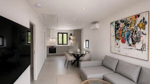 Una sala de estar moderna con un sofá gris, una mesa de centro de vidrio y un comedor con una mesa y sillas blancas.