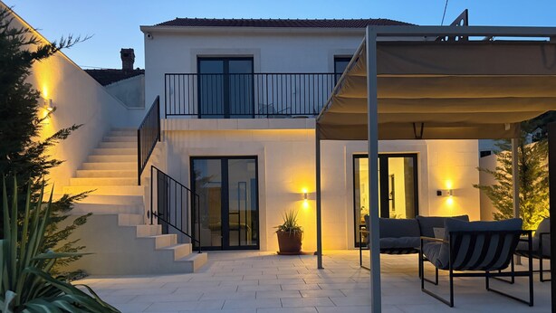 Una casa moderna de dos pisos con un porche cubierto, una escalera y mobiliario exterior.