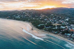 Ein Luftbild einer Küstenstadt mit Strand, Häusern und Bergen im Hintergrund.