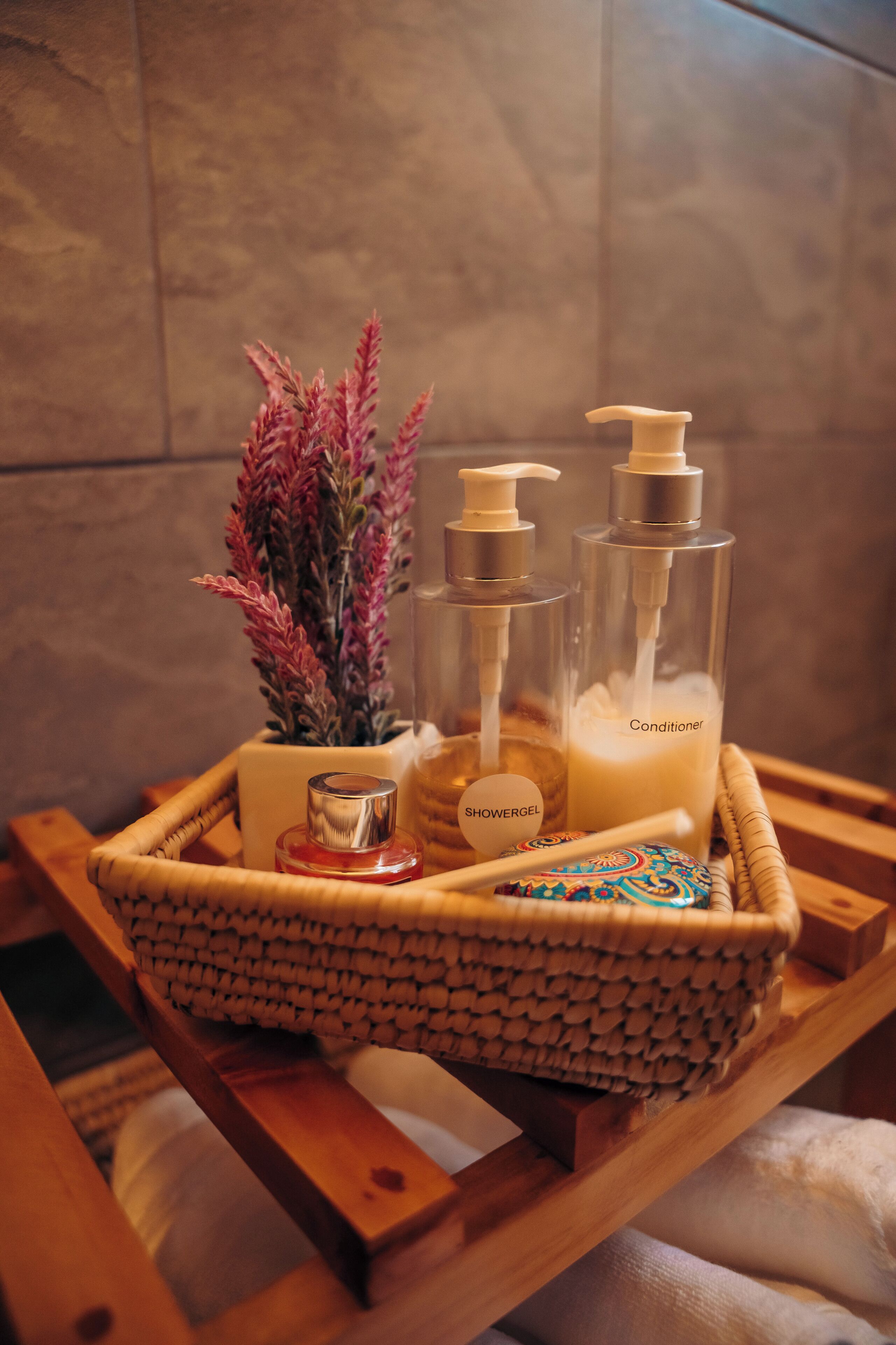 Un plateau en bois contenant une bouteille en verre étiquetée « gel douche », une bouteille transparente étiquetée « après-shampoing » et une petite plante en pot.