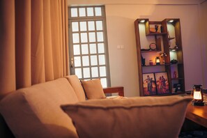 Quarto com cama, janela com cortinas, estante de livros e mesa com lanterna.