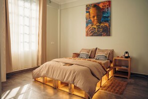 Ein Schlafzimmer mit Bett, Nachttisch, Lampe, einem Poster an der Wand und einem Fenster mit Vorhängen.
