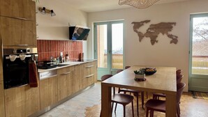 A modern kitchen with wooden cabinets, a built-in oven, and a dining area with a wooden table and chairs. - "SIGI" Cozy apartment at the foot of the Ceüse cliff (Sigoyer)