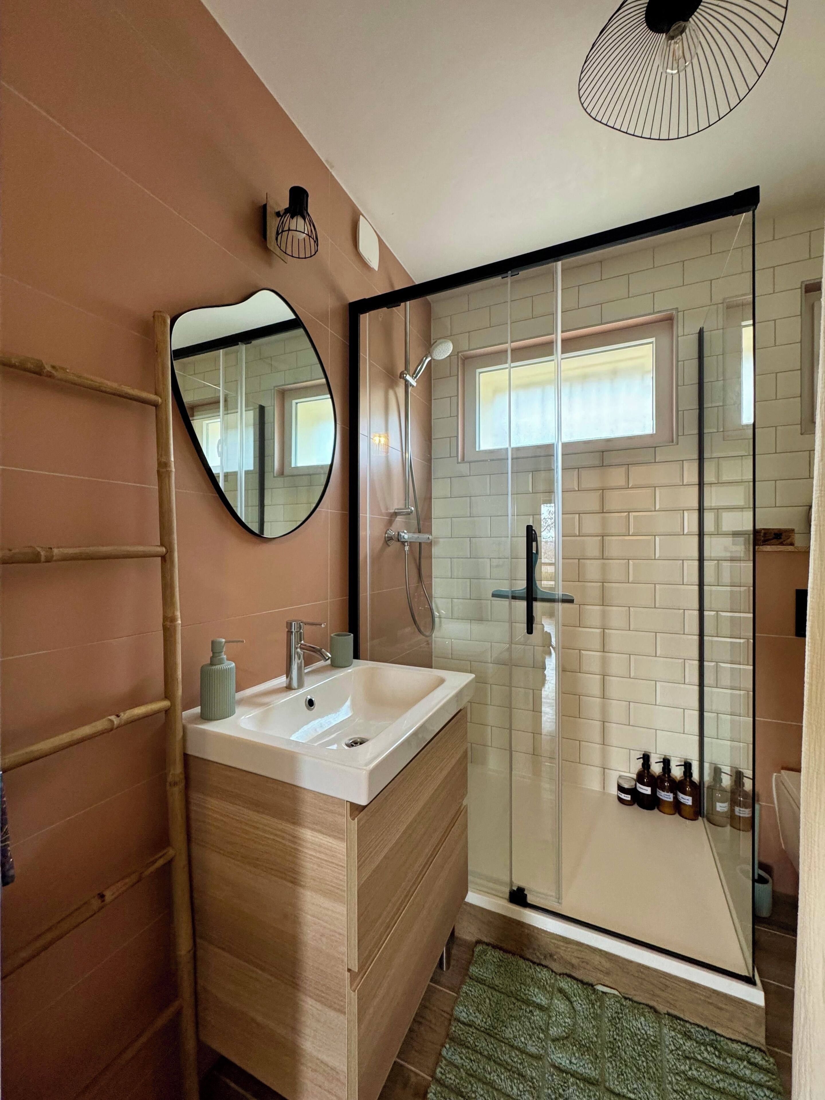 Ein Badezimmer mit Holzwaschtisch, Spiegel, Duschkabine aus Glas und kleinem Fenster.