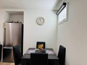 A dining area with a table, chairs, a clock, and a refrigerator.