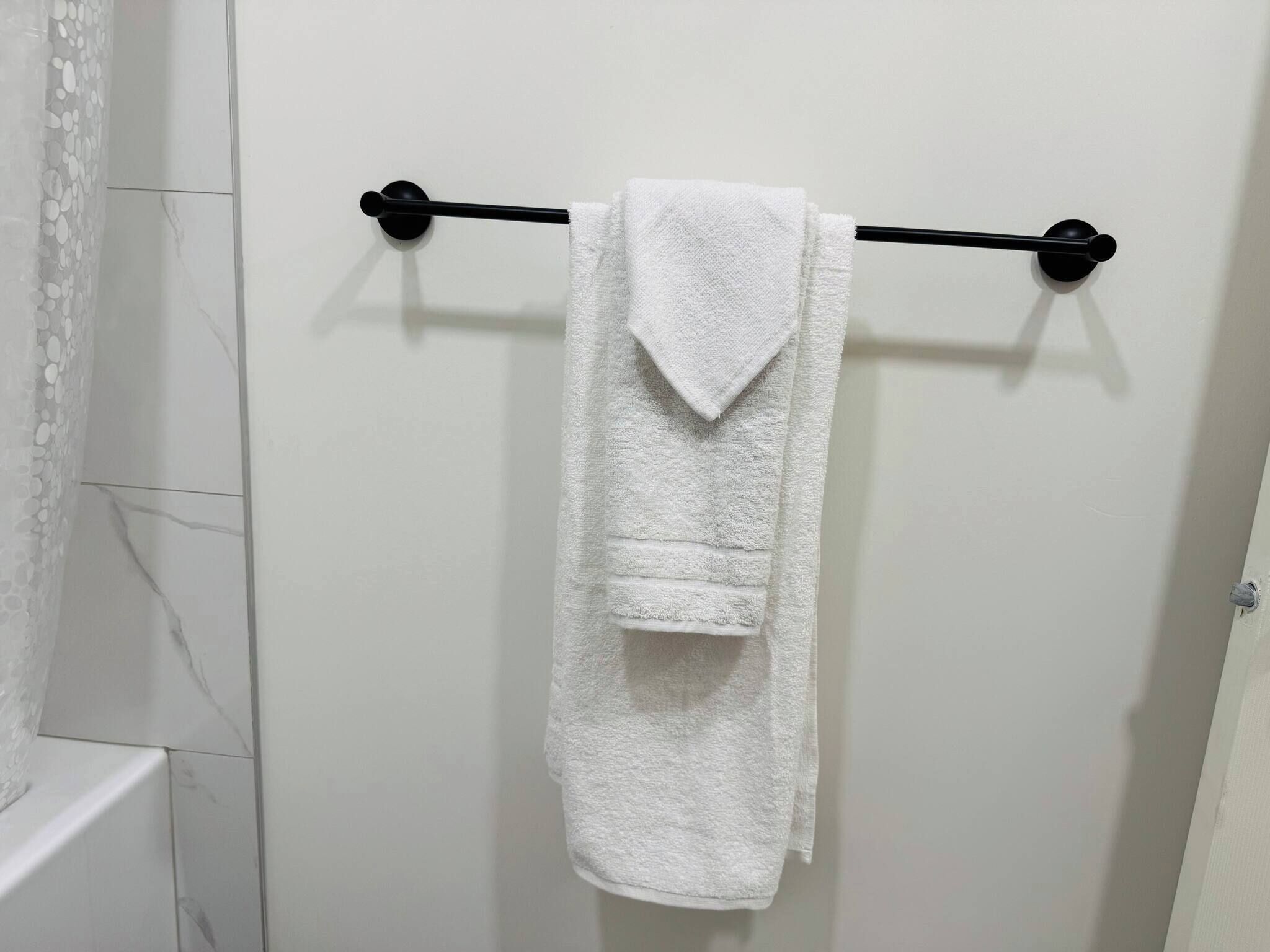 A white towel hanging on a black towel bar in a bathroom with white marble tiles.
