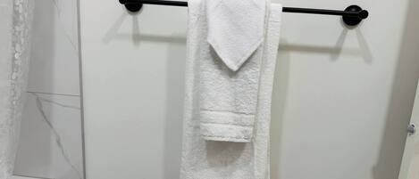 A white towel hanging on a black towel bar in a bathroom with white marble tiles.