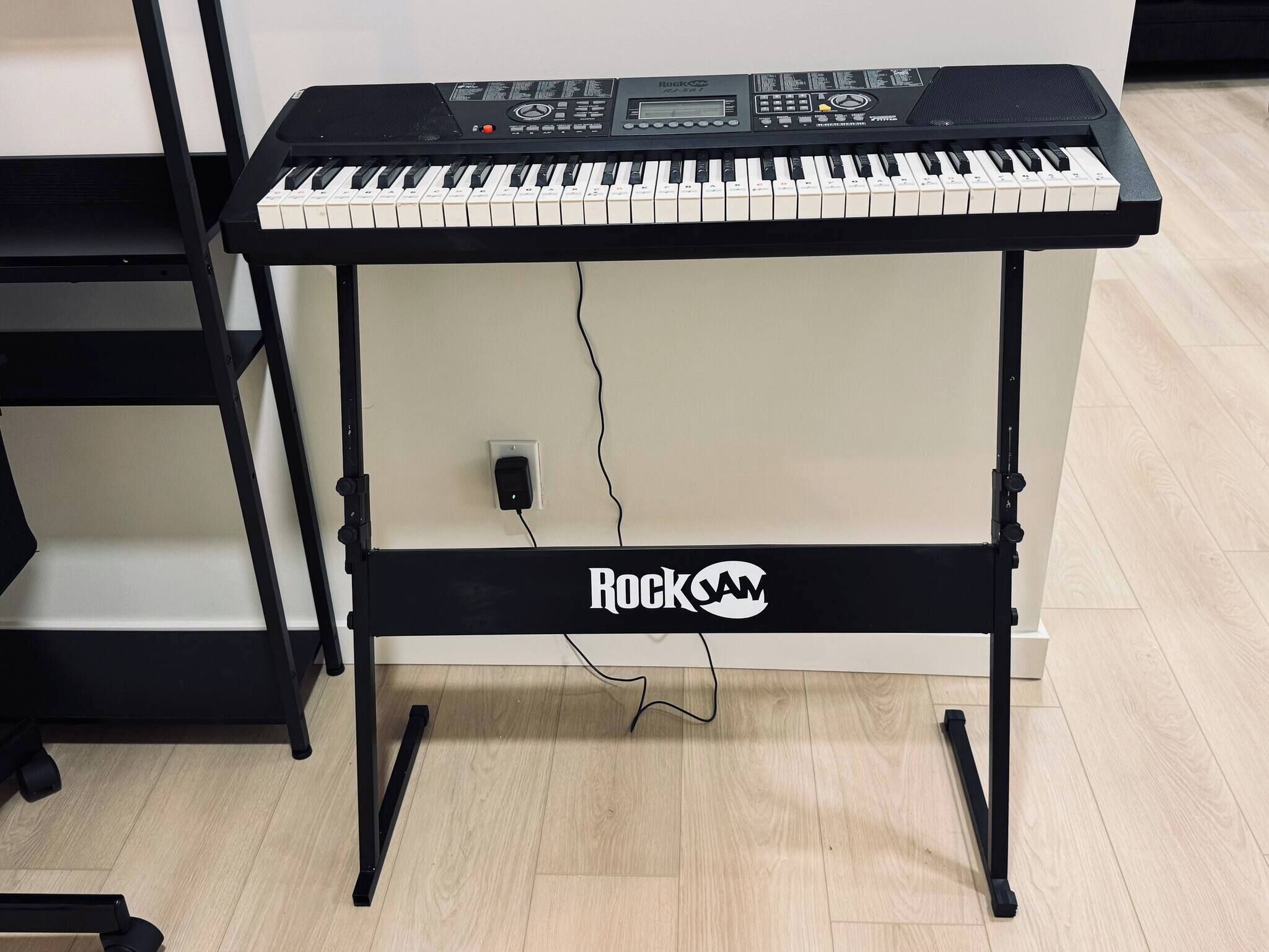 A RockJam electronic keyboard on a stand with a power outlet.