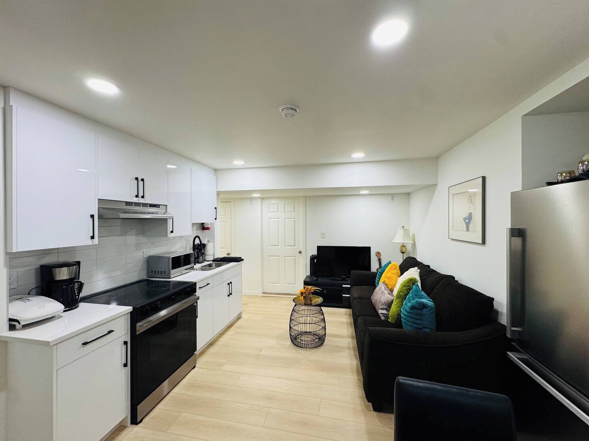 A modern kitchen with white cabinets, a black countertop, and a stainless steel refrigerator.