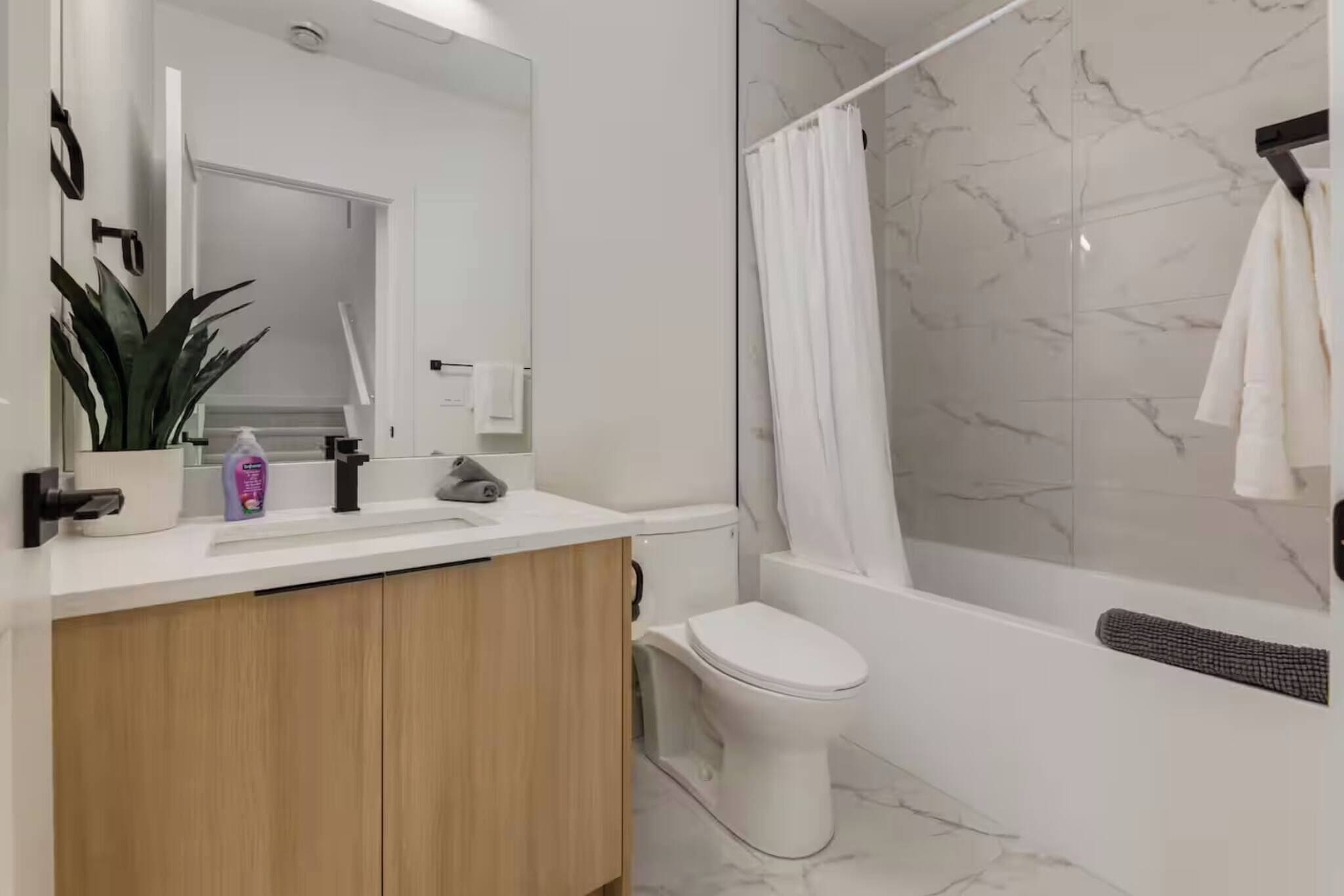 Un baño moderno con ducha de mármol, inodoro blanco y tocador de madera.