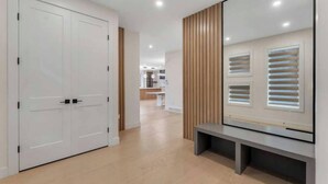 A hallway with a white door, a bench, and a wall-mounted TV.