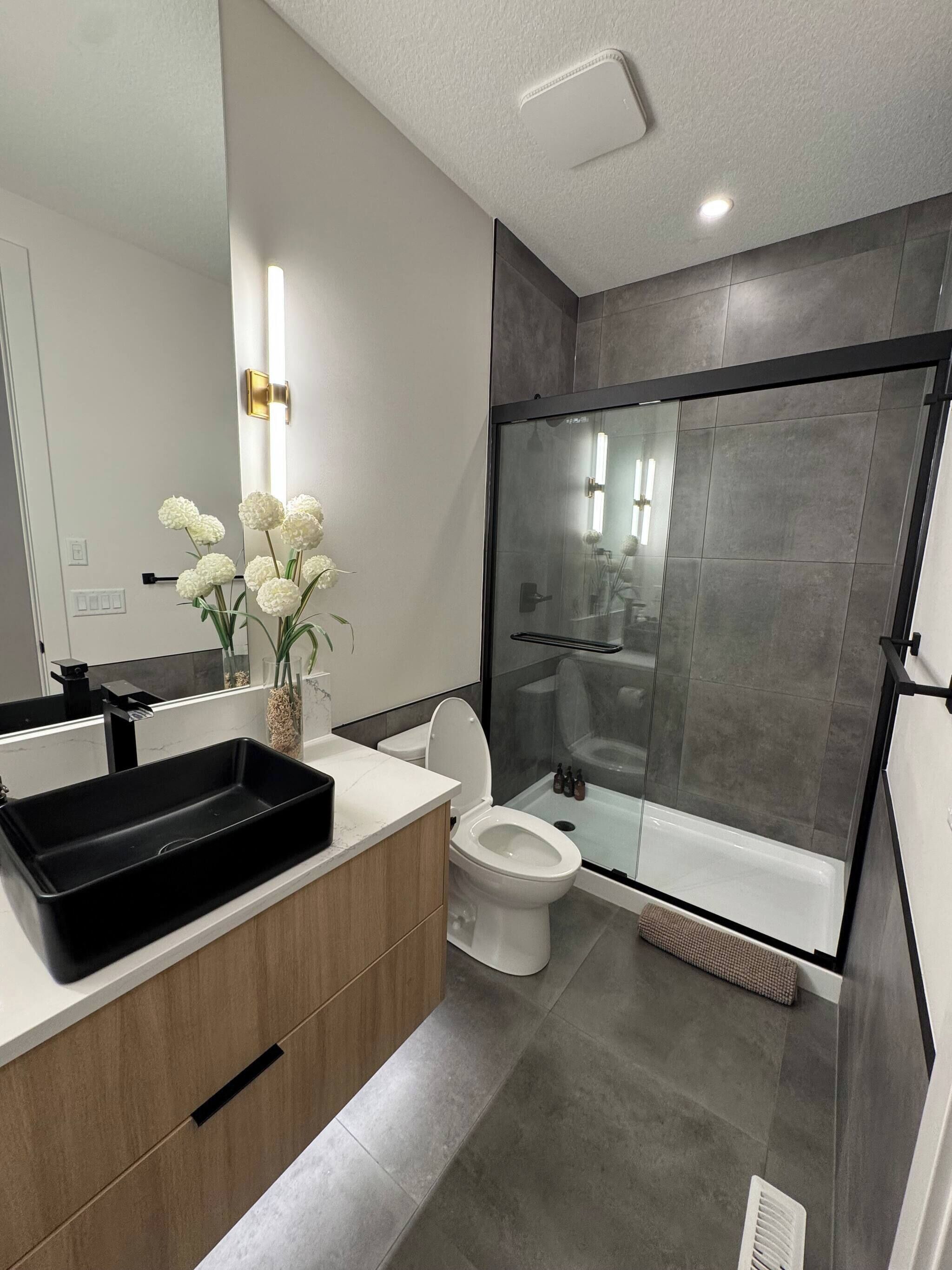 A modern bathroom with a black sink, white toilet, and a glass-enclosed shower.