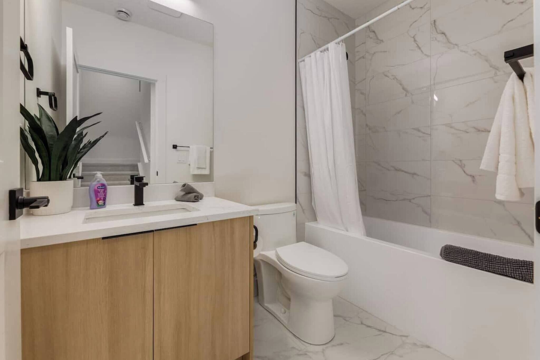 A modern bathroom with a white sink, mirror, and toilet, a shower with a marble wall, and a towel hanging on a rack.