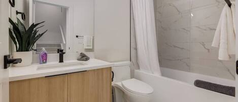 A modern bathroom with a white sink, mirror, and toilet, a shower with a marble wall, and a towel hanging on a rack.