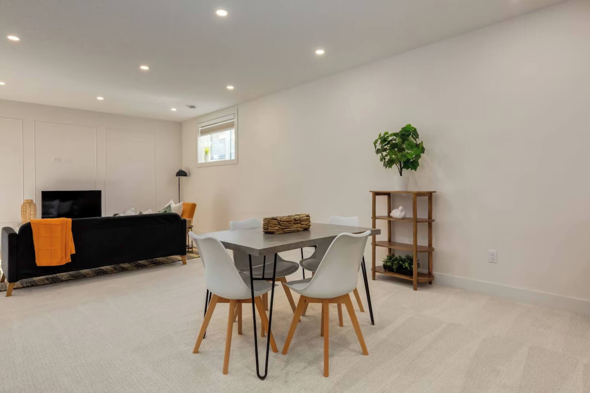 A modern living room with a sofa, TV, dining table, chairs, and a plant.
