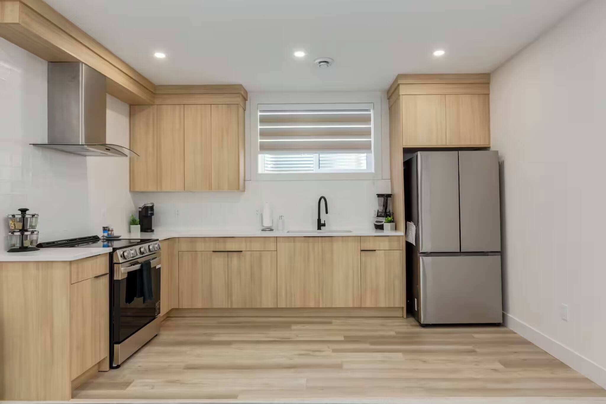 Una cocina moderna con armarios de madera, un refrigerador de acero inoxidable y una ventana con persianas.