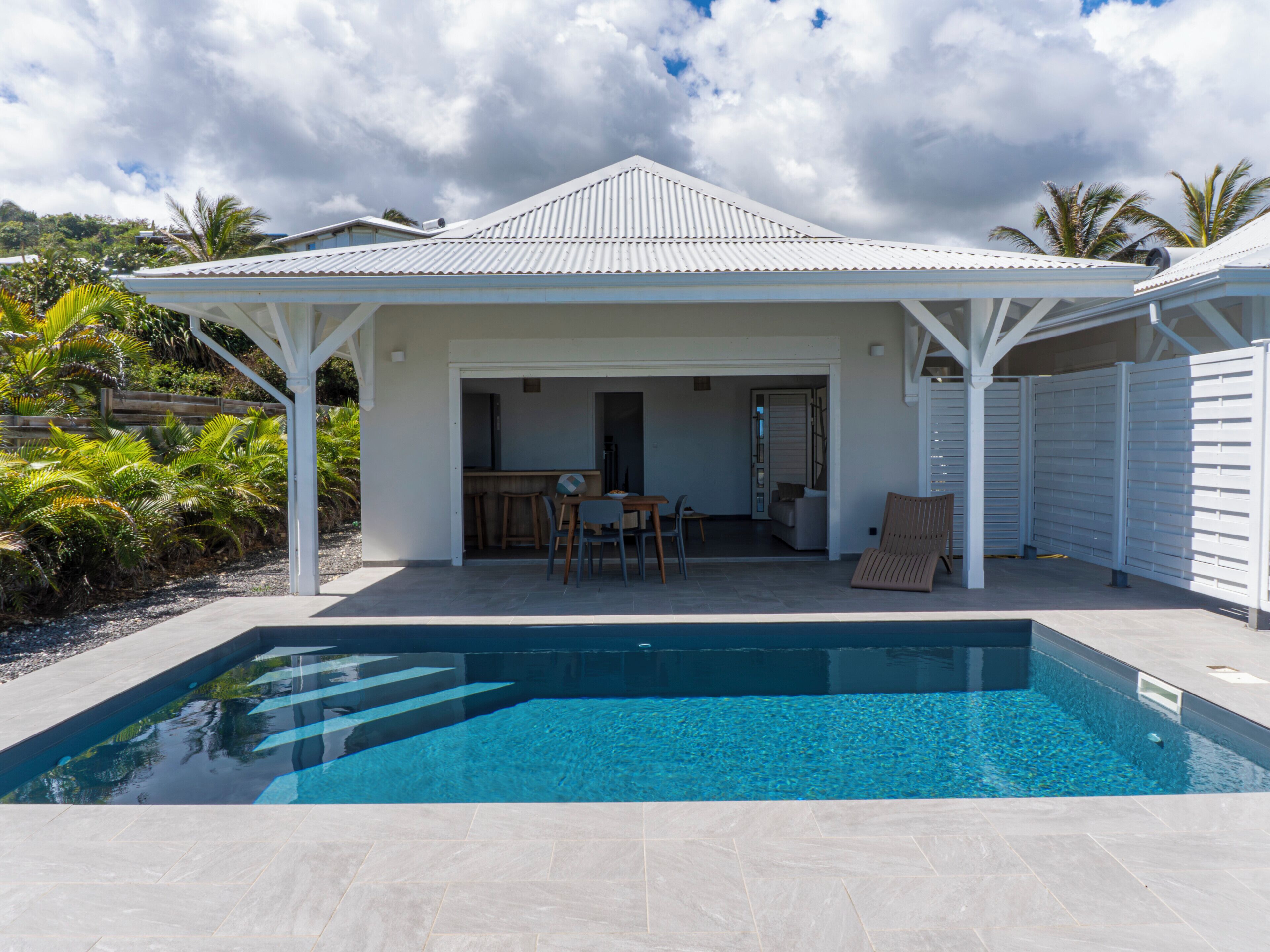 A poolside area with a covered patio, a dining area, and a view of the surrounding landscape.