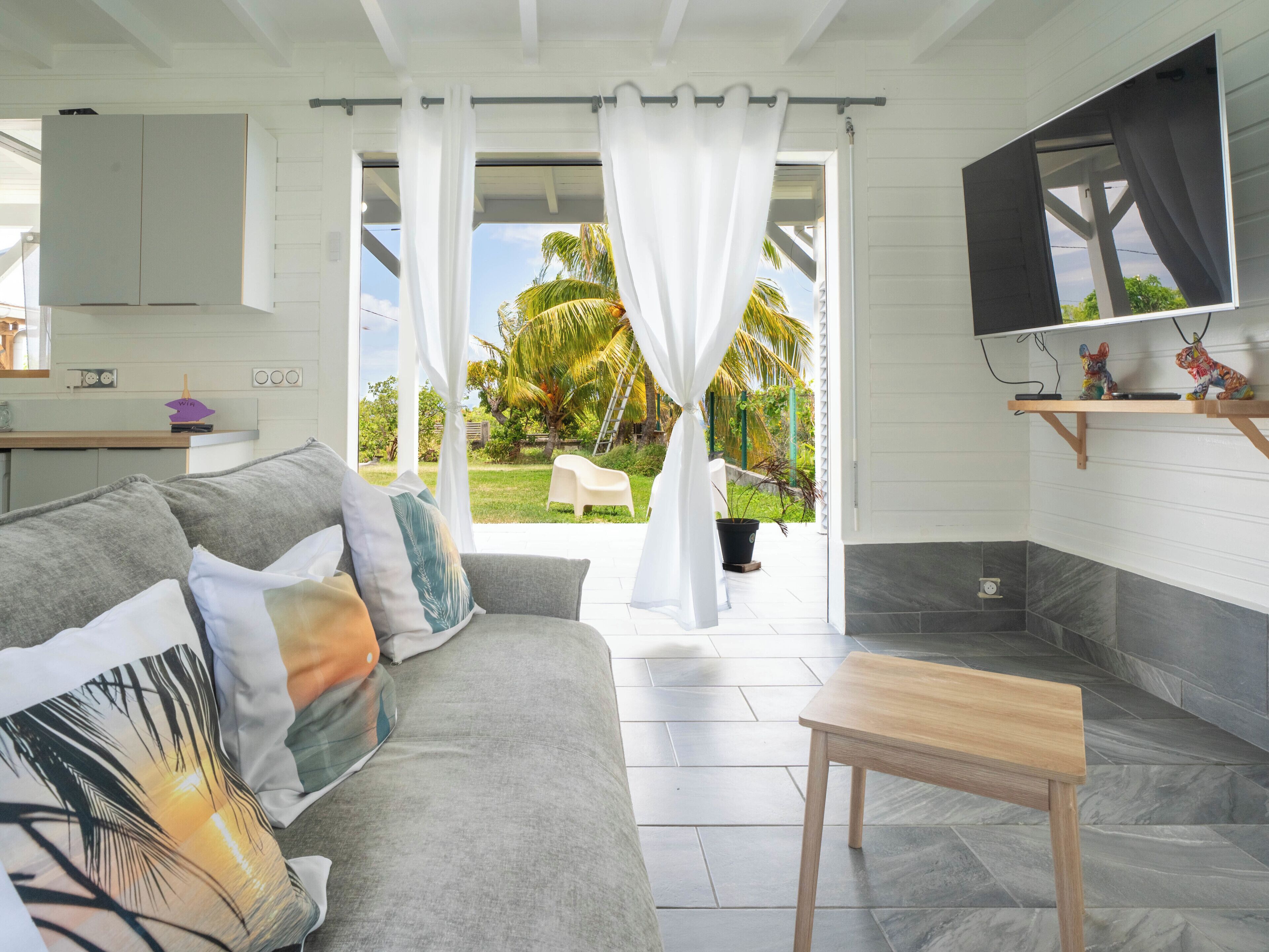 A modern living room with a grey sofa, a wooden coffee table, and a TV mounted on the wall.