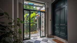 Un pasillo con piso a cuadros, una puerta verde y una puerta de cristal que da a un jardín.