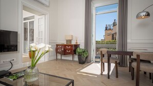 Amplia sala de estar con televisor, mesa de centro de vidrio, un florero con flores, un mueble de madera y vistas al exterior.