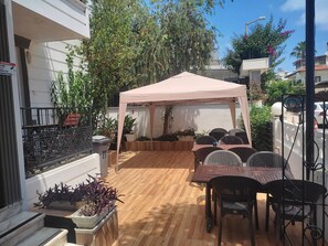 Un patio con una mesa, sillas, una carpa y plantas en macetas.