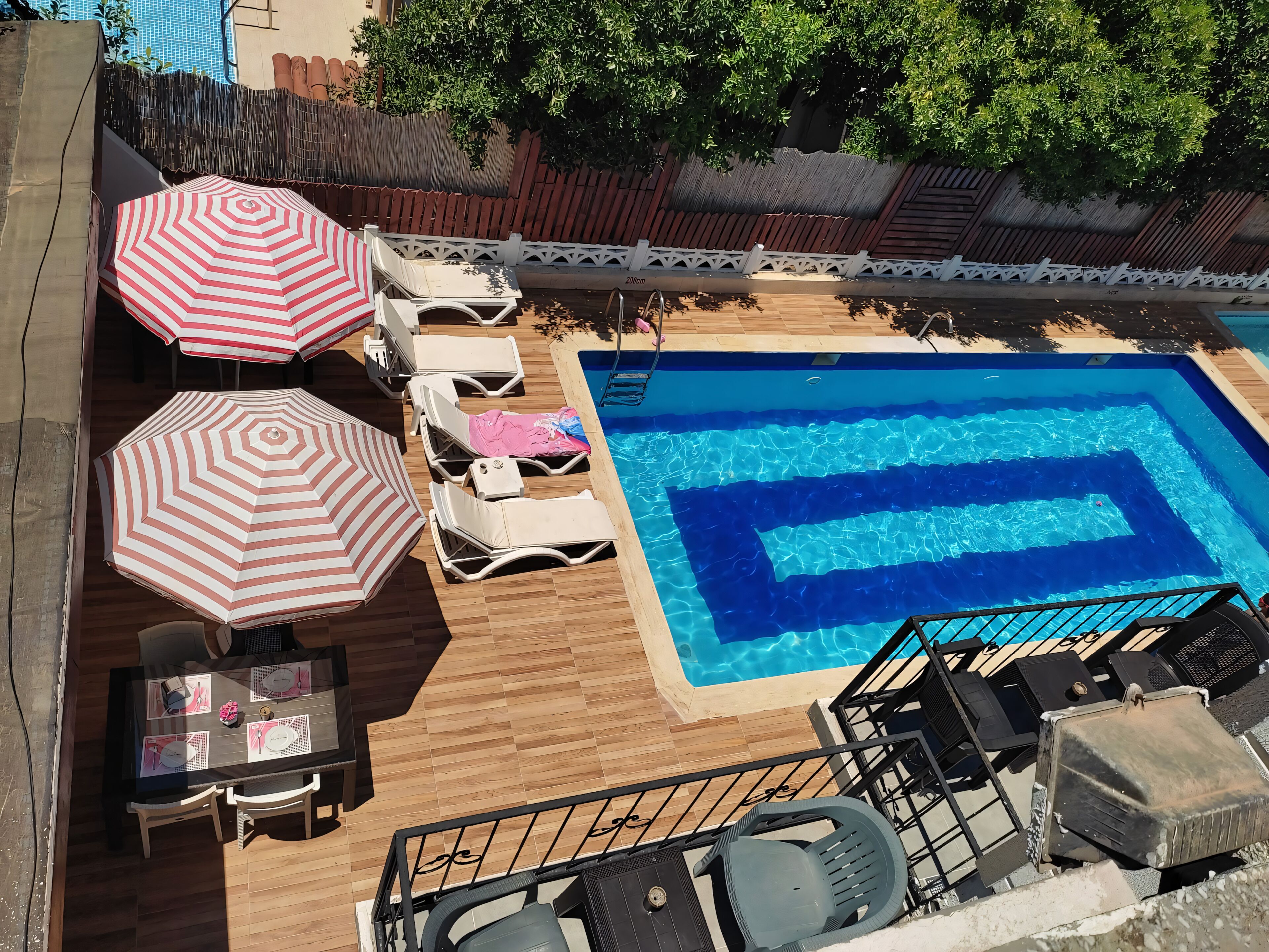 A rooftop pool area with lounge chairs, umbrellas, and a dining table.