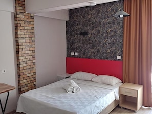 A hotel room with a brick accent wall, a red headboard, a bed with white bedding, a nightstand, and a lamp.