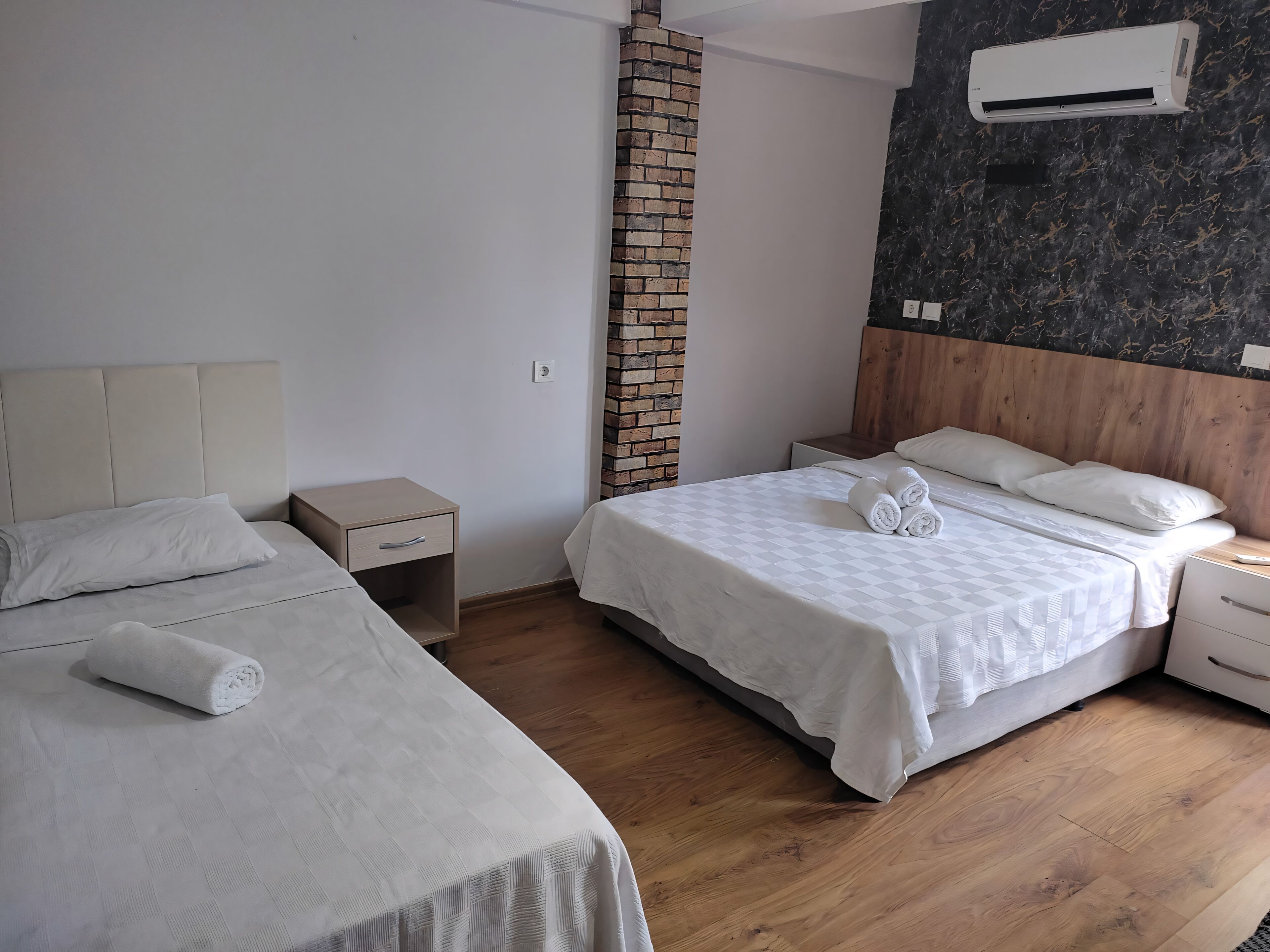 A hotel room with two beds, a brick accent wall, a marble-patterned wall, and an air conditioning unit.