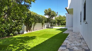 Un cortile con prato curato, vialetto in pietra e pareti bianche.
