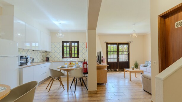 Una cucina moderna con mobili bianchi, un'area pranzo con tavolo e sedie, un piccolo angolo salotto con un divano e una scala in legno.