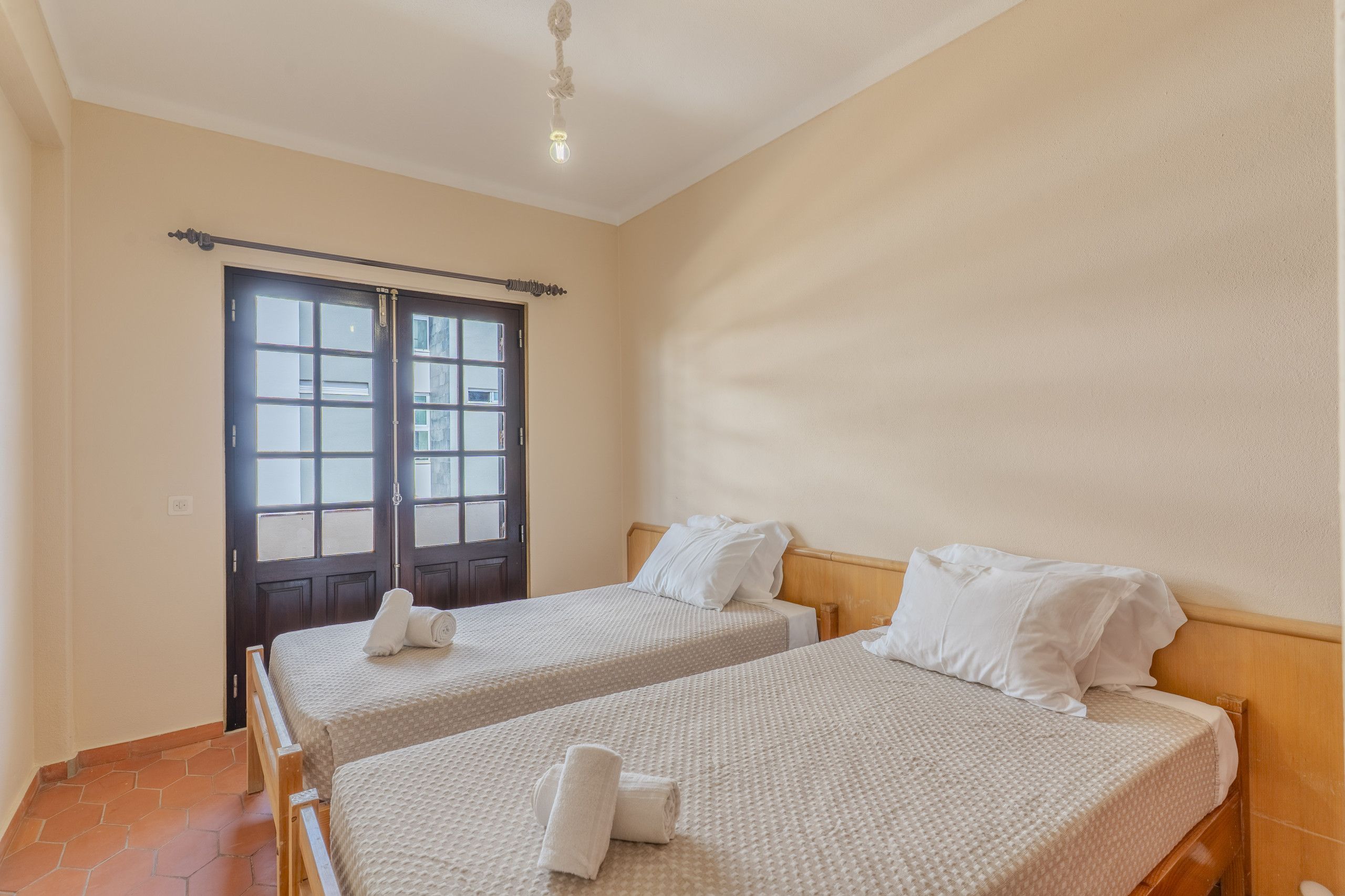 Een kamer met twee bedden, een houten hoofdbord, een deur met glaspanelen en een lamp aan het plafond.