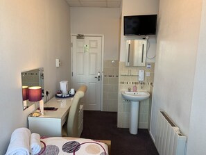 A hotel room with a bed, a desk with a lamp, a TV mounted above the bed, a bathroom with a sink and mirror, and a door with a lock. - Austins Self Service Guest House (Cardiff)