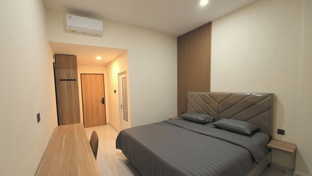 A bedroom with a bed, bedside tables, a wooden bench, an air conditioning unit, and a door. - Unika Coliving Vibes Syariah (Pekanbaru)