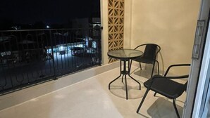 A balcony with a glass table and two chairs, a decorative wall panel, and a view of the cityscape at night. - Unika Coliving Vibes Syariah (Pekanbaru)