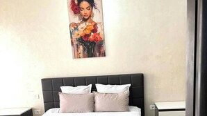 Un dormitorio con cama, dos mesitas de noche, un cuadro en la pared y una puerta.