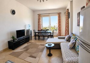 A living room with a TV, sofa, dining table, and a water dispenser.