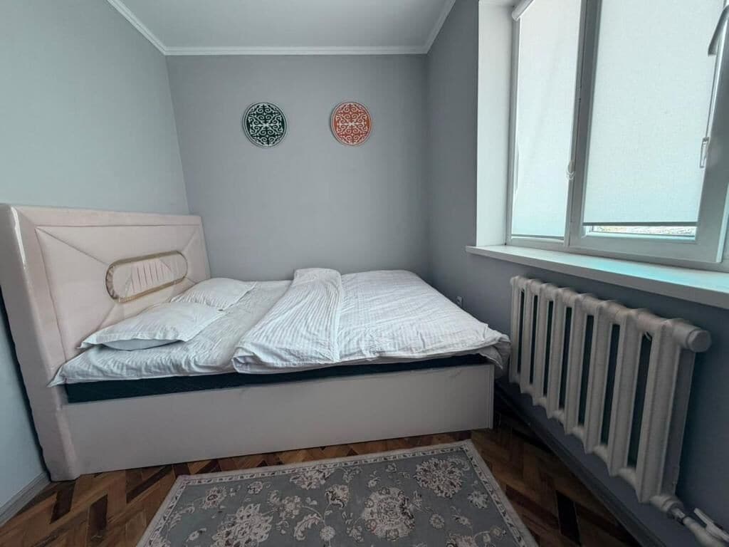 A bedroom with a bed, a radiator, a window, and two wall decorations.