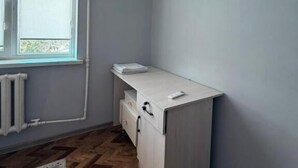 Una habitación con radiador, ventana, escritorio blanco y suelo con diseño de espiga.