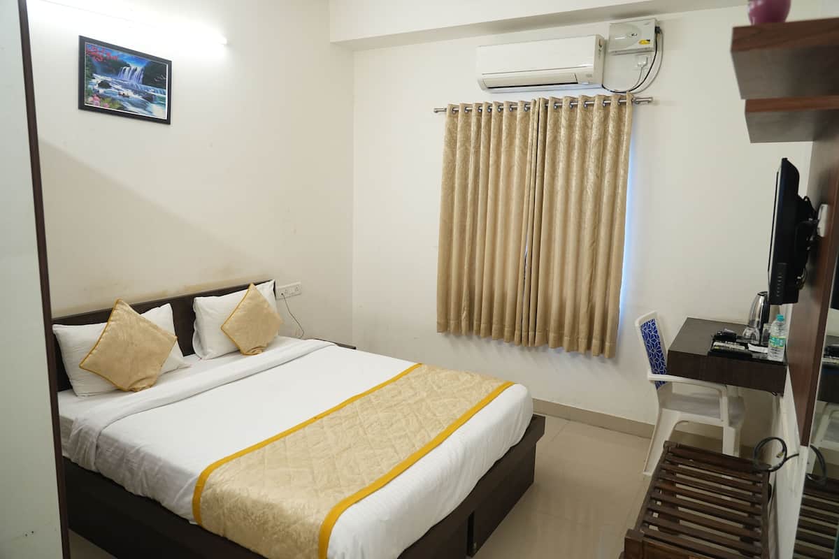 A hotel room with a bed, a desk, a chair, an air conditioning unit, and a curtain.