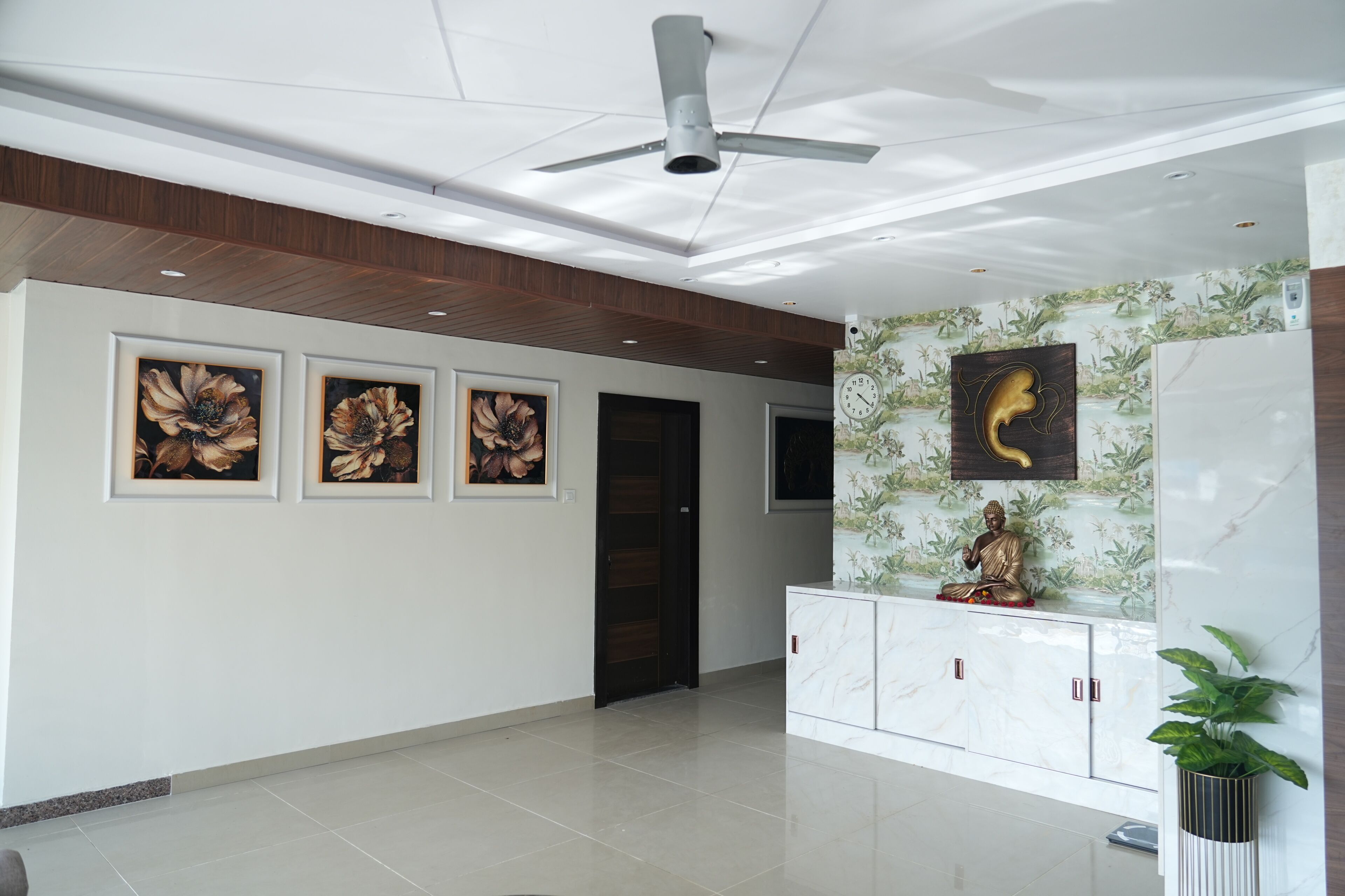 A modern lobby with a ceiling fan, framed floral artwork, a Buddha statue, and a marble cabinet.