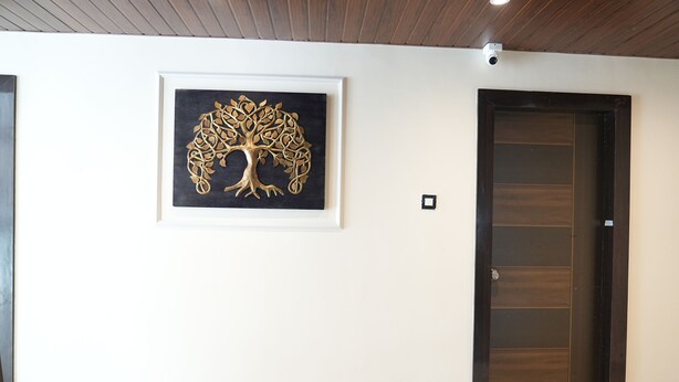 A hallway with a framed artwork of a tree, a dark wooden door, and a light-colored wall. - I Cloud Elite Suites (Bengaluru)