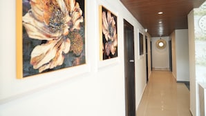 A corridor with framed floral artwork on the walls, a wooden ceiling, and a clock on the wall. - I Cloud Elite Suites (Bengaluru)