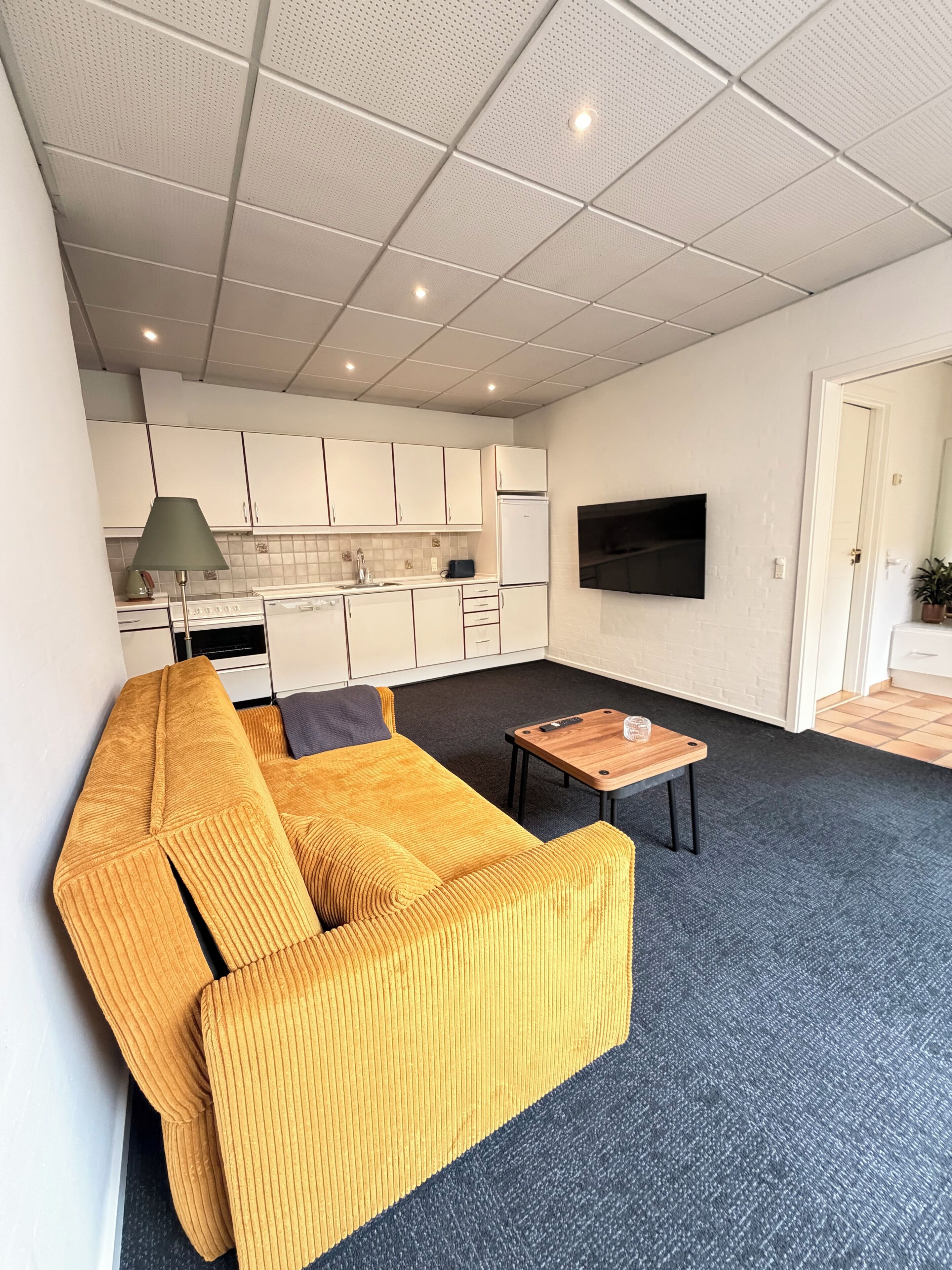 A modern living room with a sofa, a coffee table, and a kitchen area in the background.