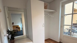 Une pièce dotée d’un grand miroir, d’une armoire blanche, d’une plante en pot, d’un sol carrelé et d’une porte donnant sur un espace extérieur.